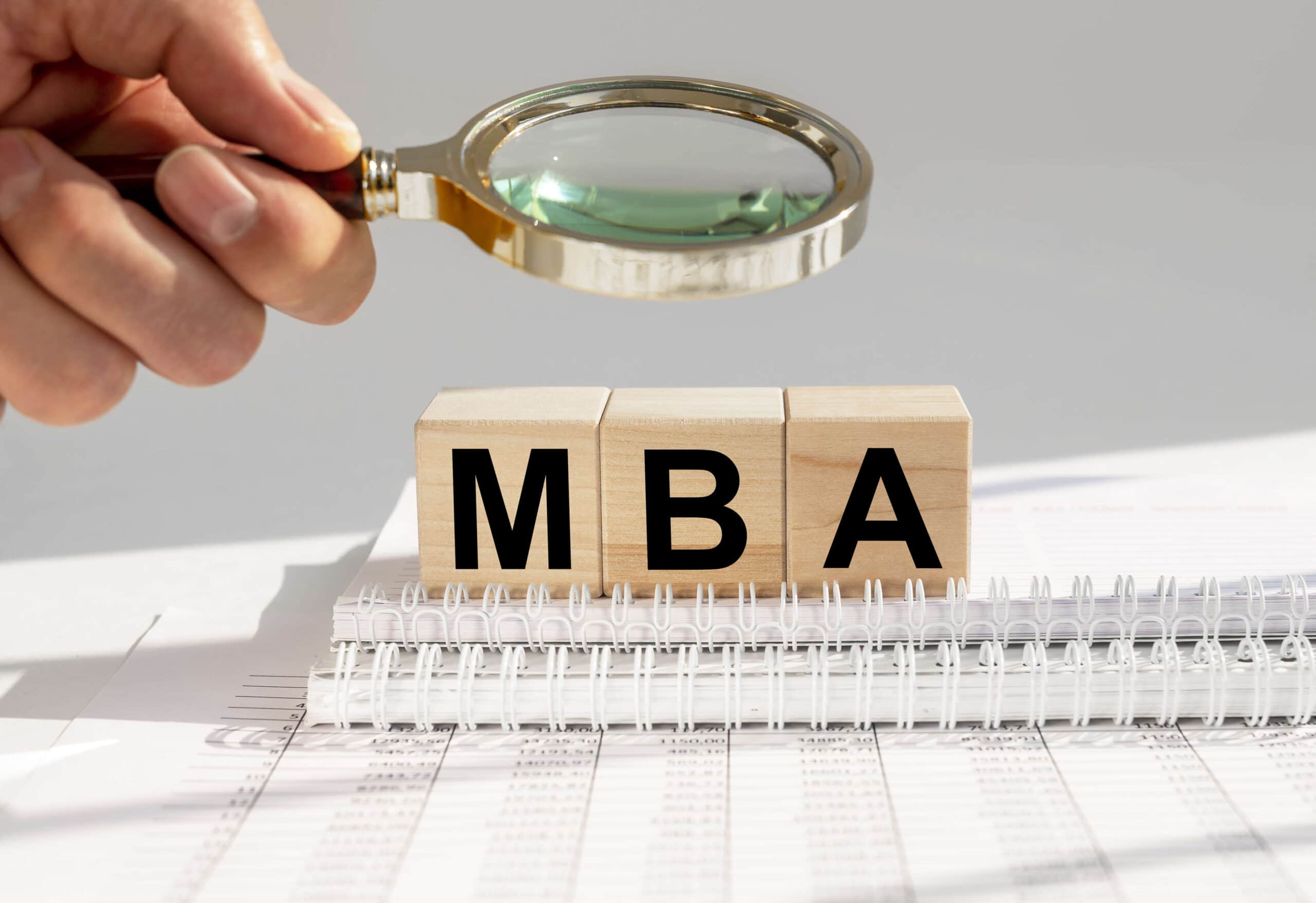 A magnifying glass over wooden blocks of the letters "MBA"